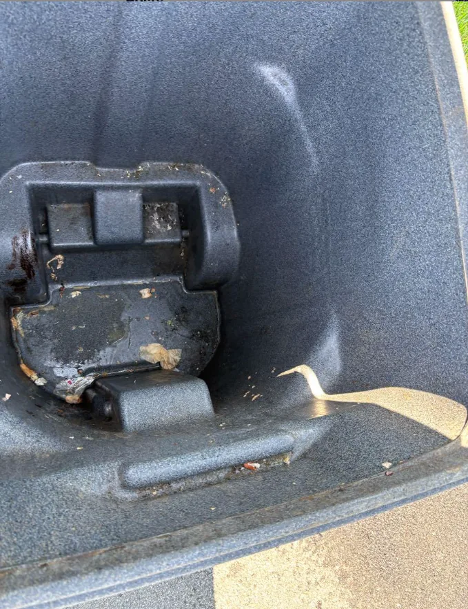 Caked-on food residue and debris around the lid hinge and floor of a grey trash cart