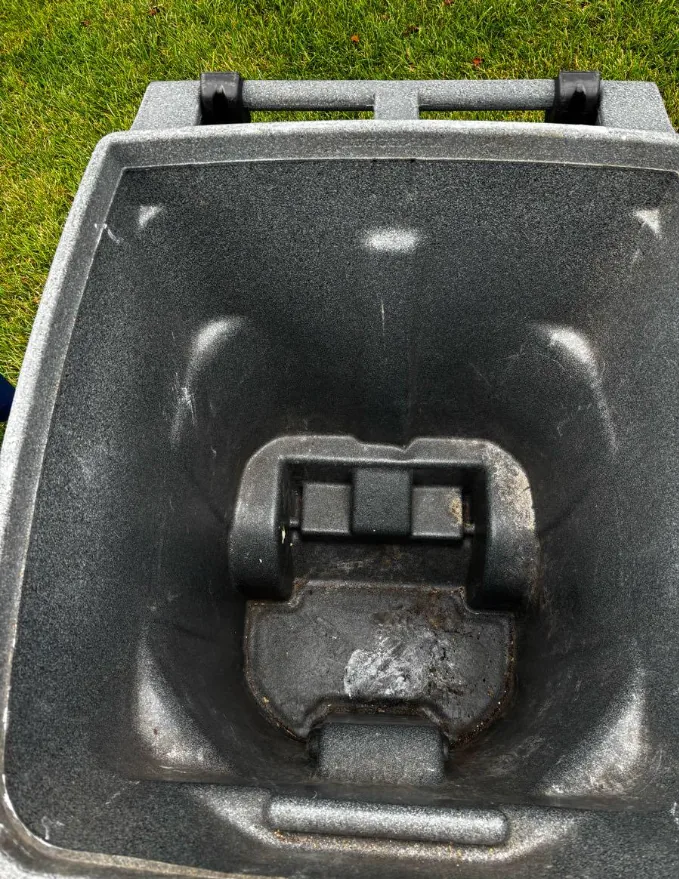 Dried residue built up around the base and lift bar of a grey trash cart